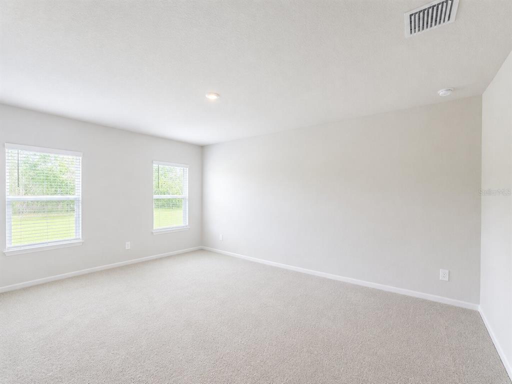 An empty bedroom with beige carpet, light-colored walls, and two windows — 810 172ND COURT E, BRADENTON, FL