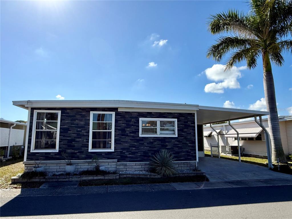 A single-story home with dark stone siding, white-trimmed windows, and an attached carport — 82257 3RD AVENUE N UNIT 257, PINELLAS PARK, FL