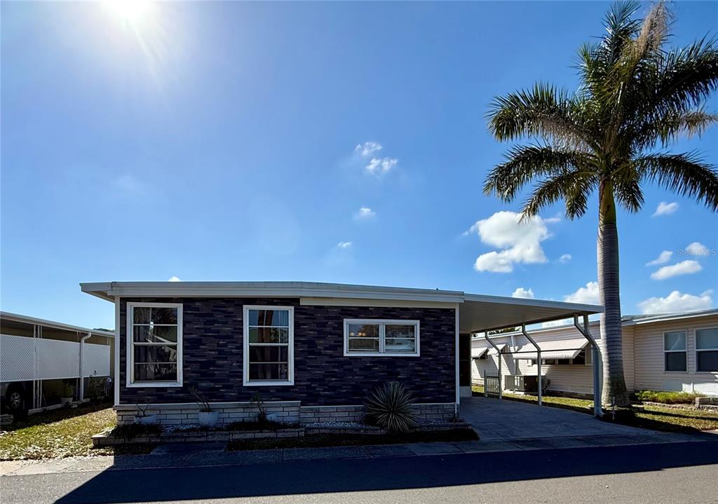 A single-story manufactured home with dark stone siding, a carport, and a palm tree — 82257 3RD AVENUE N UNIT 257, PINELLAS PARK, FL