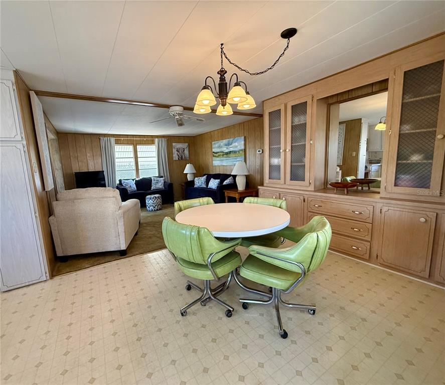 A dining area with green swivel chairs and a round table sits before a living room — 82257 3RD AVENUE N UNIT 257, PINELLAS PARK, FL