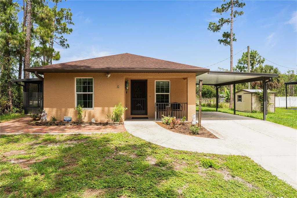 A single-story tan house features a brown roof, a front porch, and an attached carport — 3241 TROPICAIRE BOULEVARD, NORTH PORT, FL
