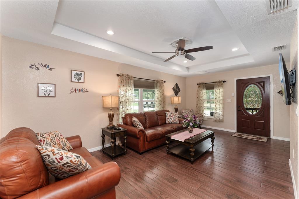 A living room features leather sofas, a tray ceiling, and wood-look tile flooring — 3241 TROPICAIRE BOULEVARD, NORTH PORT, FL