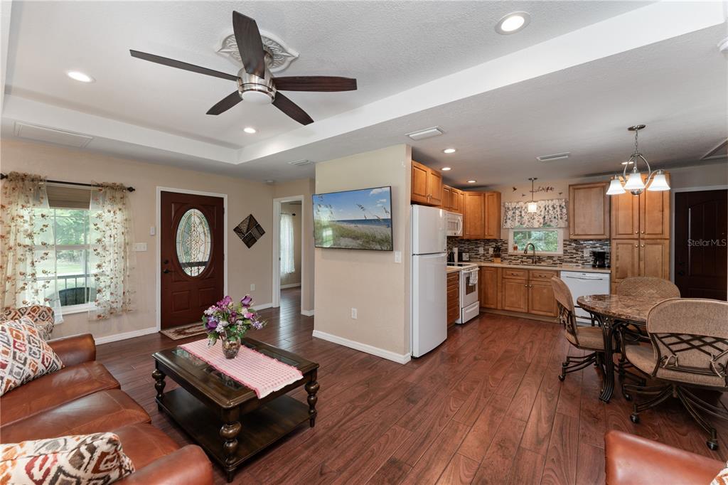 An open-concept living room and kitchen feature wood-look flooring, wooden cabinets, and a ceiling fan — 3241 TROPICAIRE BOULEVARD, NORTH PORT, FL