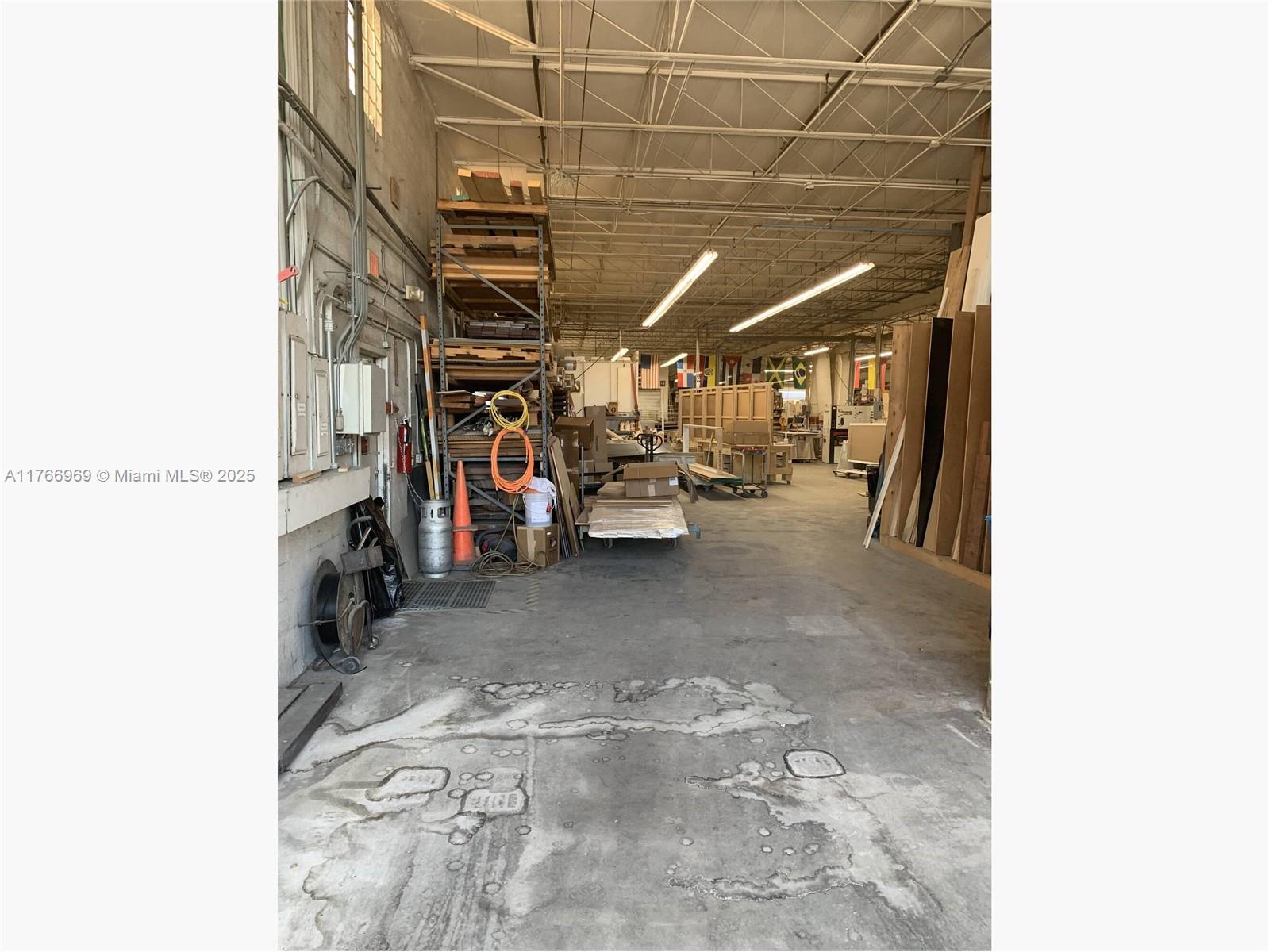 A spacious industrial workshop features concrete floors, high ceilings, and storage racks for lumber — 1677 W 31st Pl # 1677, Hialeah FL 33012, HIALEAH, FL