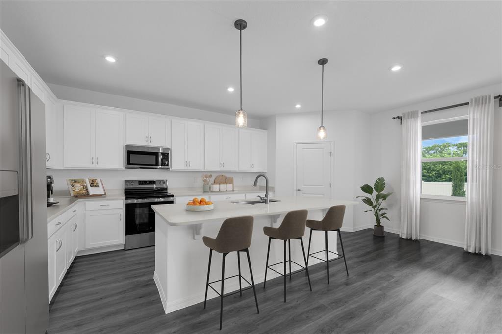 A modern kitchen features white cabinets, a central island with bar stools, and dark flooring — 1422 W DUNBLANE WAY NE, PALM BAY, FL