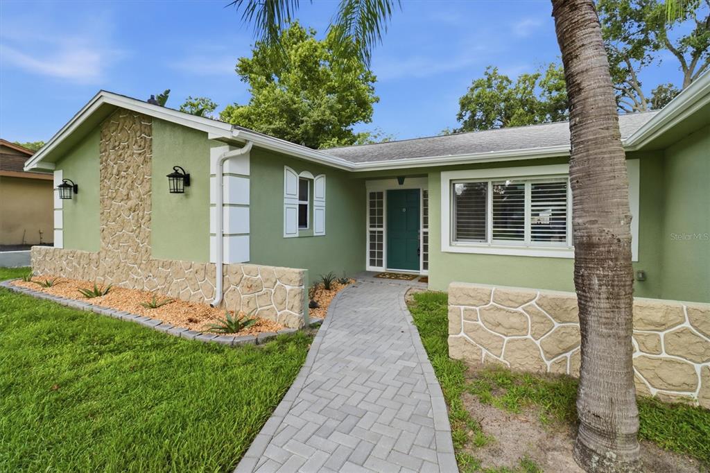 A green single-story house features a stone facade, a paved walkway, and a palm tree — 644 PEACHWOOD DRIVE, ALTAMONTE SPRINGS, FL