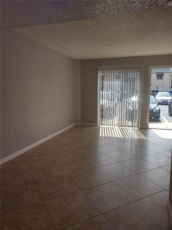 An empty room with beige tile flooring, a popcorn ceiling, and sliding glass patio doors — 4149 S SEMORAN BOULEVARD UNIT 17, ORLANDO, FL