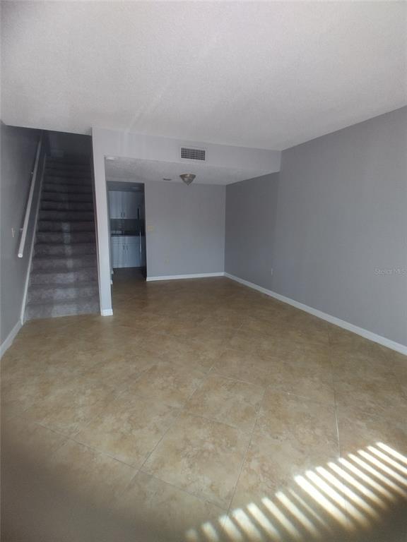 An interior view shows a tiled living area with a staircase and a kitchen beyond — 4149 S SEMORAN BOULEVARD UNIT 17, ORLANDO, FL