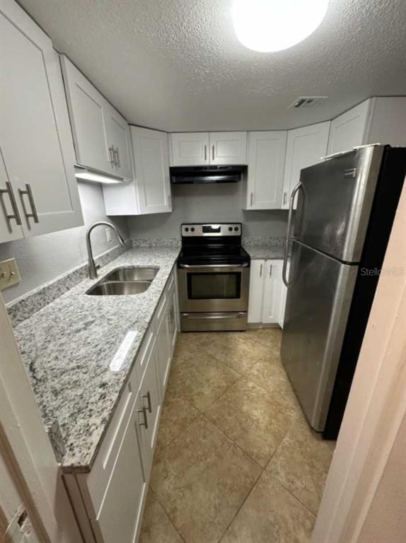 A kitchen features white cabinets, granite countertops, stainless steel appliances, and tile flooring — 4149 S SEMORAN BOULEVARD UNIT 17, ORLANDO, FL