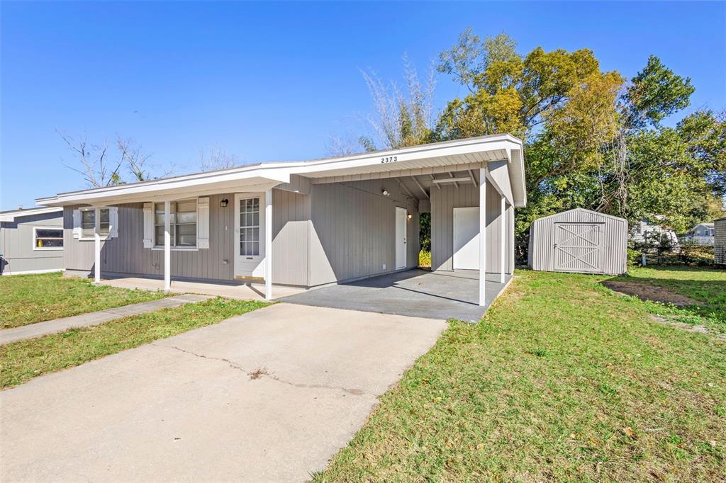 A gray single-story house features a front carport, a concrete driveway, and a storage shed — 2373 FAIRGREN AVENUE, DELTONA, FL