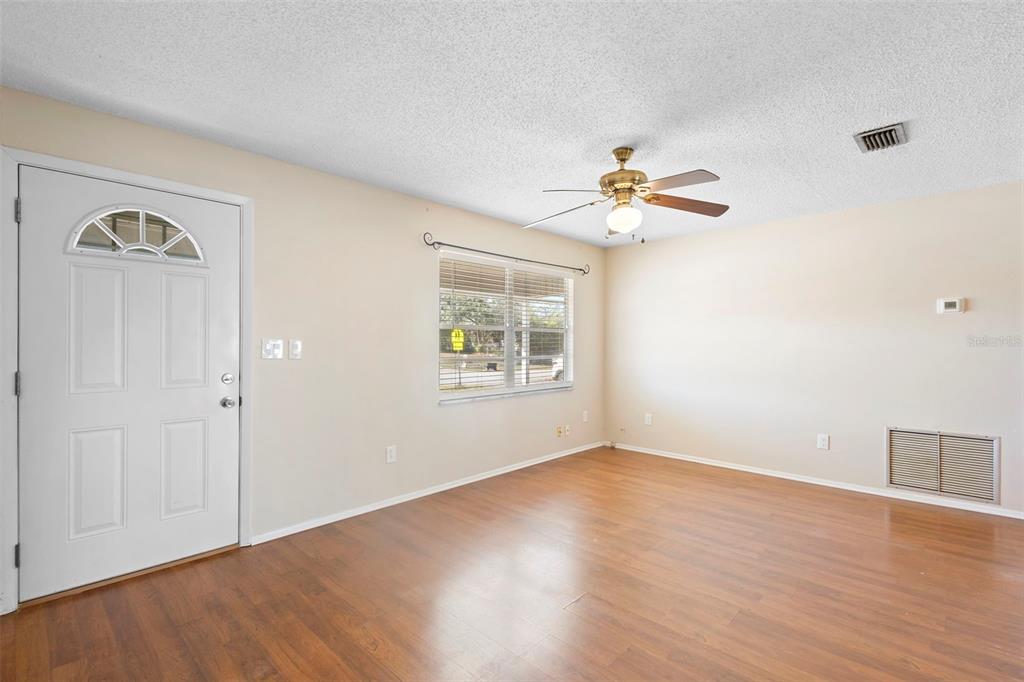 An empty room features wood-look flooring, a ceiling fan, a window, and a white door — 2373 FAIRGREN AVENUE, DELTONA, FL