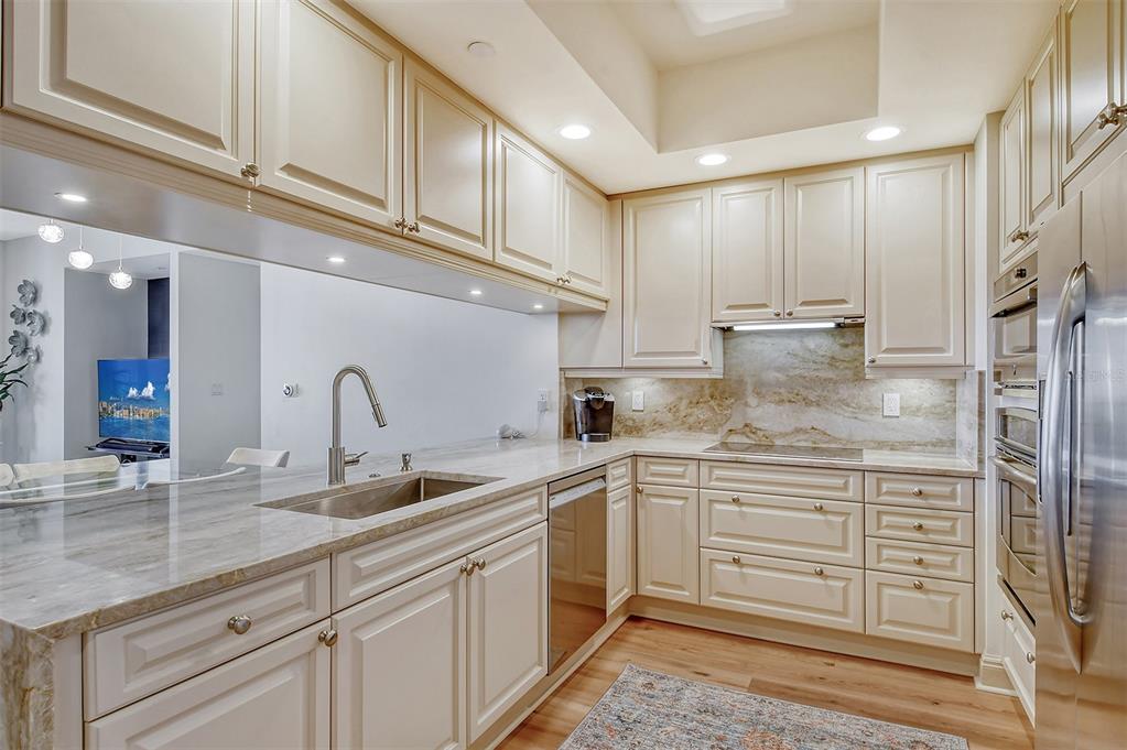 A kitchen features cream-colored cabinets, stone countertops, stainless steel appliances, and wood-look flooring — 50 CENTRAL AVENUE UNIT 15B, SARASOTA, FL