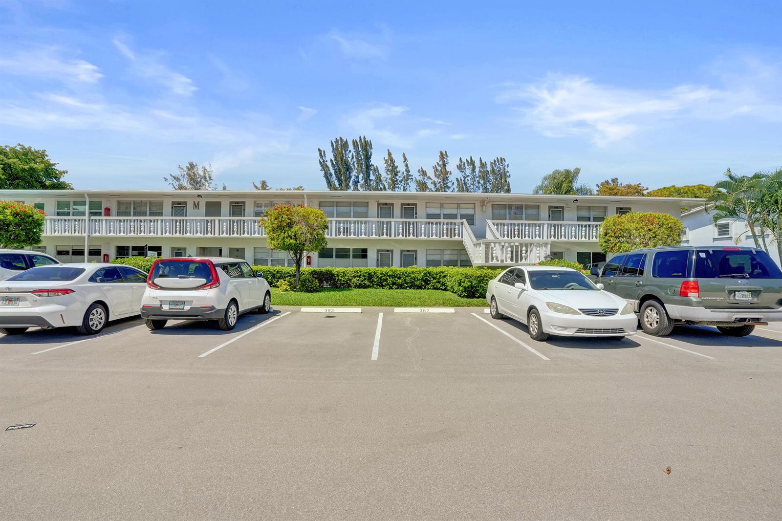 A two-story apartment building features a parking lot with several cars in the foreground — 392 Durham Circle # M, Deerfield Beach FL 33442, DEERFIELD BEACH, FL