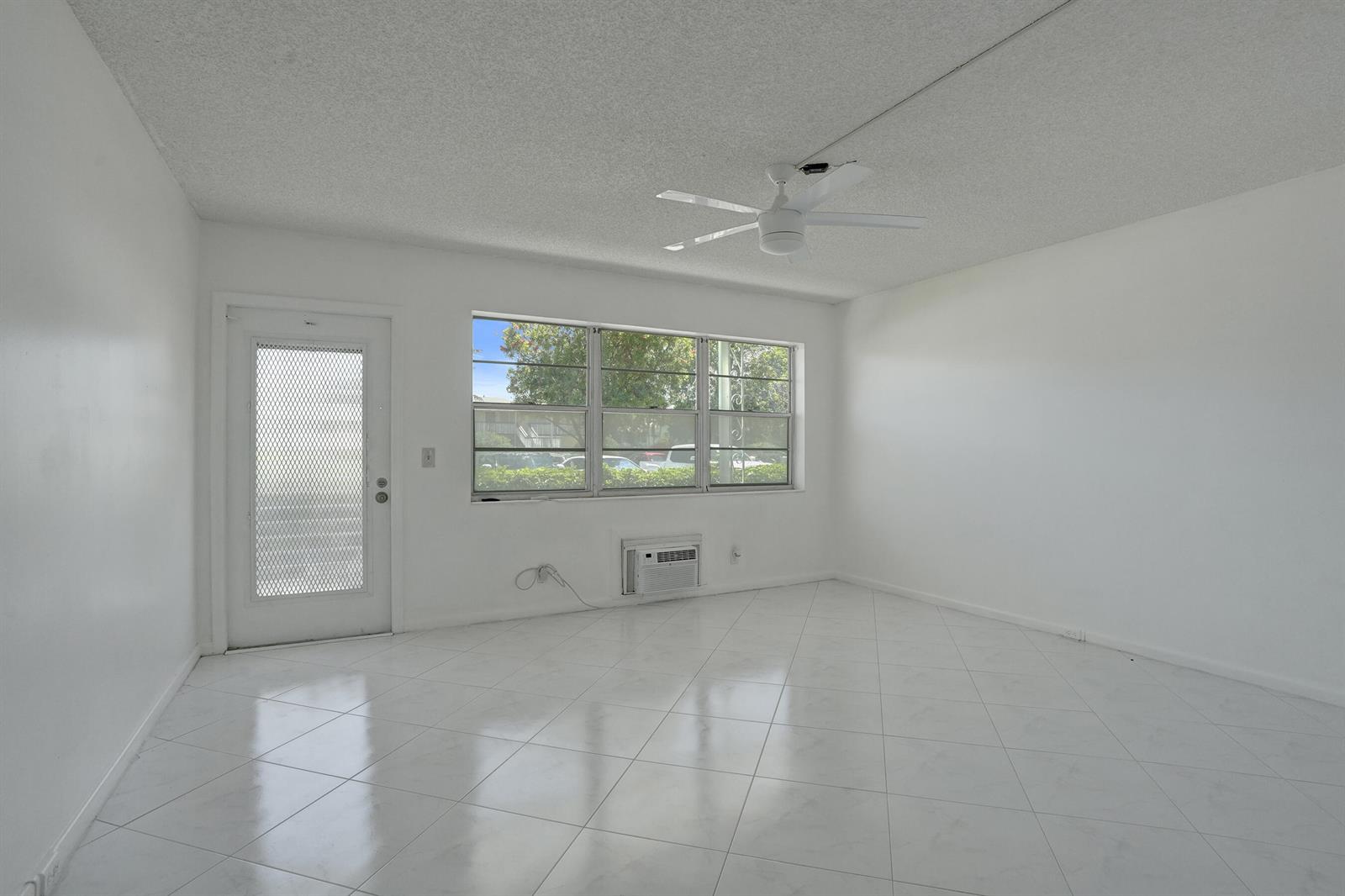 An empty room features white walls, white tile flooring, a ceiling fan, and a window — 392 Durham Circle # M, Deerfield Beach FL 33442, DEERFIELD BEACH, FL