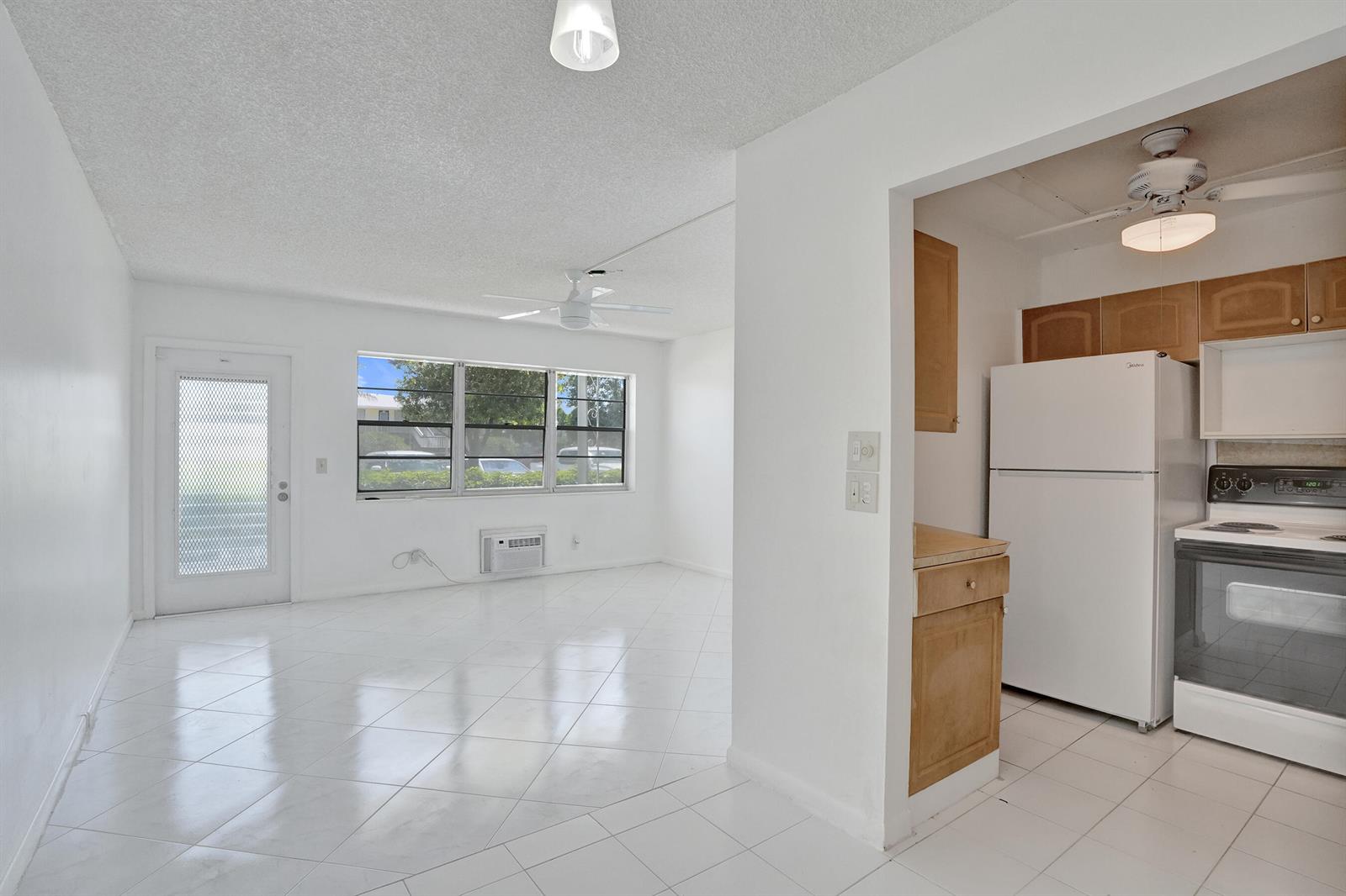 A bright living area with white tile floors connects to a kitchen with wooden cabinets — 392 Durham Circle # M, Deerfield Beach FL 33442, DEERFIELD BEACH, FL
