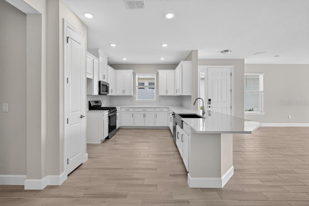 A modern kitchen features white cabinetry, quartz countertops, stainless steel appliances, and light wood flooring — 3946 IMMACOLATA WAY, WESLEY CHAPEL, FL