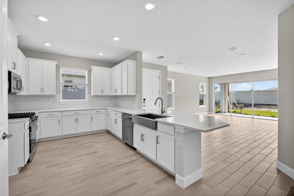 A modern kitchen features white cabinets, a farmhouse sink, stainless appliances, and light wood flooring — 3946 IMMACOLATA WAY, WESLEY CHAPEL, FL