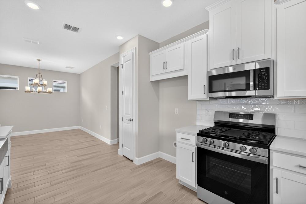 A kitchen with white cabinets, stainless steel appliances, and light wood-look tile flooring — 3946 IMMACOLATA WAY, WESLEY CHAPEL, FL