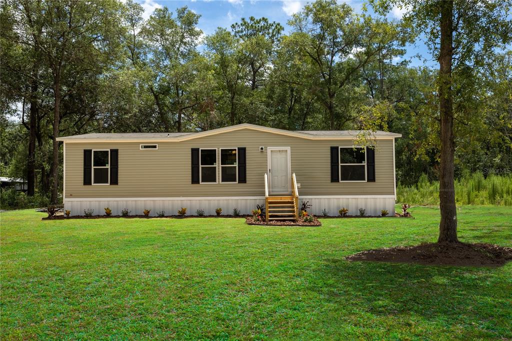 A single-story manufactured home with tan siding and black shutters sits on a grassy lot — 104 JACKSON AVENUE, INTERLACHEN, FL