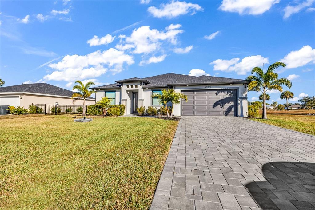 A single-story house with a gray garage, paved driveway, and palm trees under a blue sky — 25272 DOREDO DRIVE, PUNTA GORDA, FL