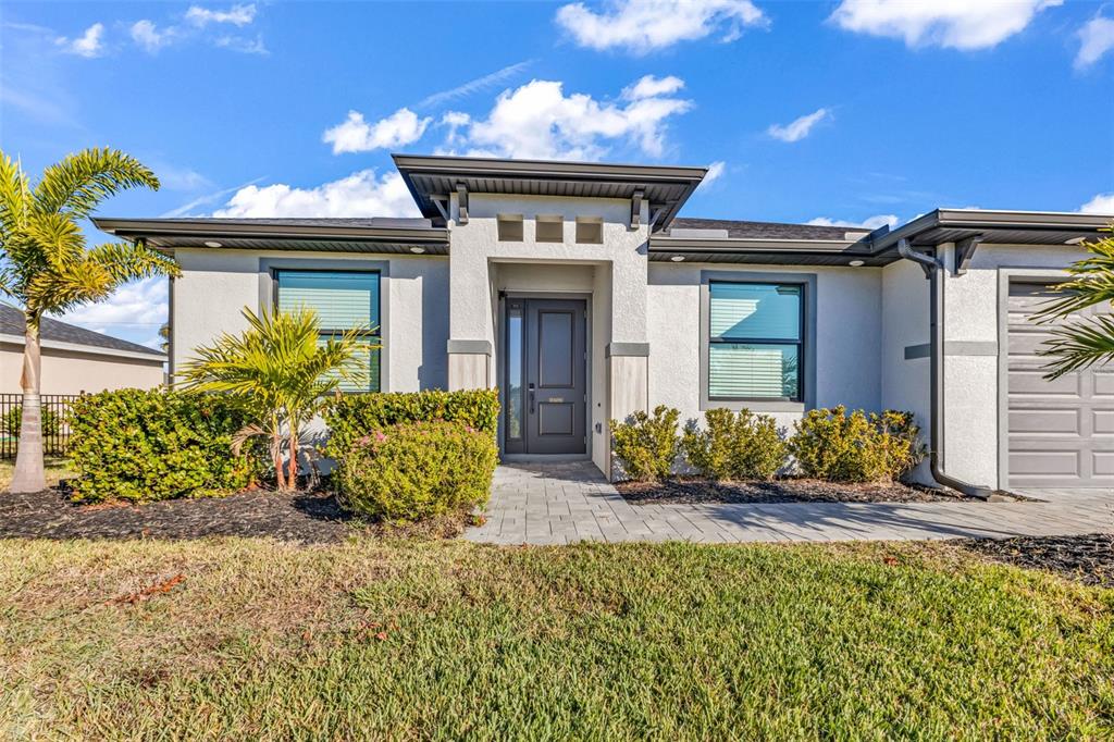The exterior of a modern one-story house features a gray front door and stone walkway — 25272 DOREDO DRIVE, PUNTA GORDA, FL