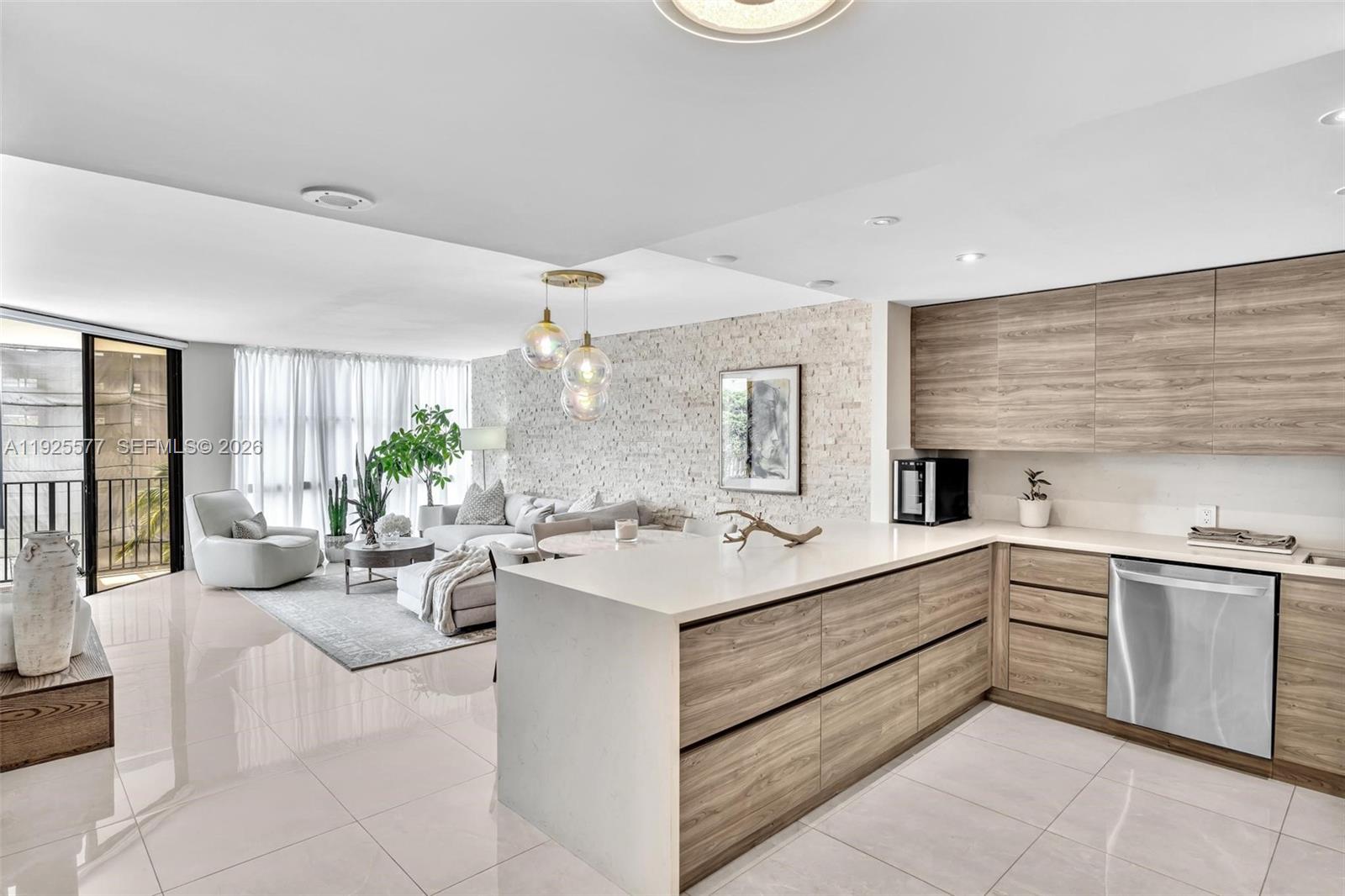 A modern open-concept kitchen and living area features wood-grain cabinetry, stone wall accents, and tile flooring — 1865 Brickell Ave # A703, Miami FL 33129, MIAMI, FL
