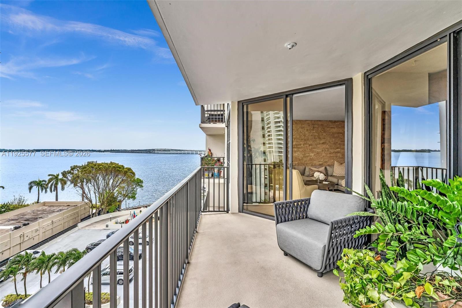 A balcony with a gray armchair and potted plants overlooks a bay and bridge — 1865 Brickell Ave # A703, Miami FL 33129, MIAMI, FL