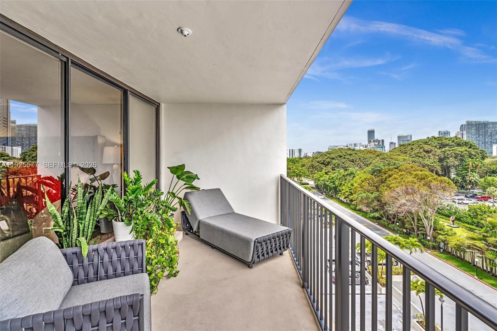 A balcony features a gray lounge chair, outdoor seating, potted plants, and a city view — 1865 Brickell Ave # A703, Miami FL 33129, MIAMI, FL