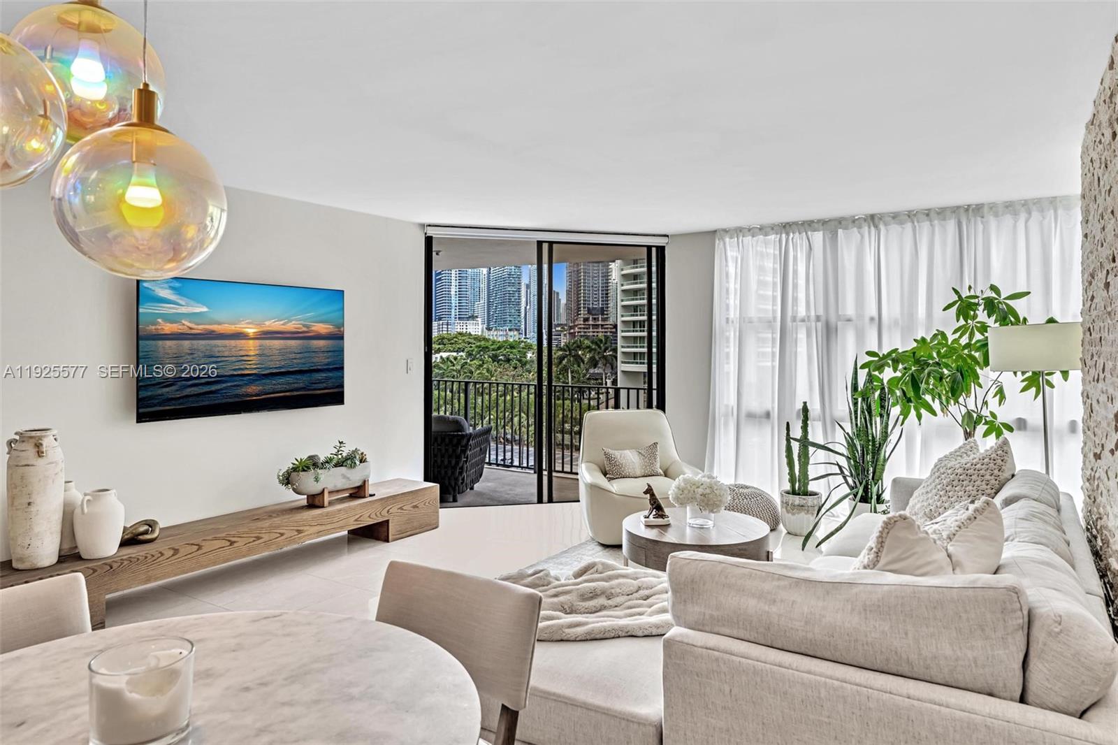 A bright living room features a television, a balcony with city views, and neutral furniture — 1865 Brickell Ave # A703, Miami FL 33129, MIAMI, FL