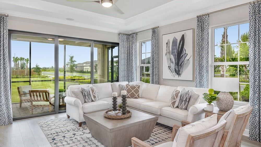A bright living room features a white sectional sofa, a square coffee table, and large windows — 7531 MOONBEAM AVENUE, SARASOTA, FL
