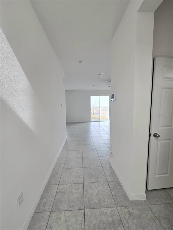 A hallway with light-colored tile flooring leads toward an open living area with sliding doors — 1603 GARDINER STREET, HAINES CITY, FL