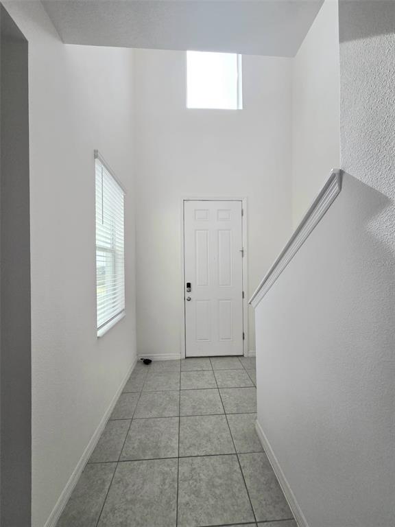 A bright entryway features white walls, tile flooring, a front door, and a high ceiling — 1603 GARDINER STREET, HAINES CITY, FL