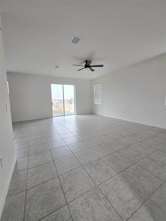 A spacious, empty living room features light-colored tile flooring, white walls, and a ceiling fan — 1603 GARDINER STREET, HAINES CITY, FL