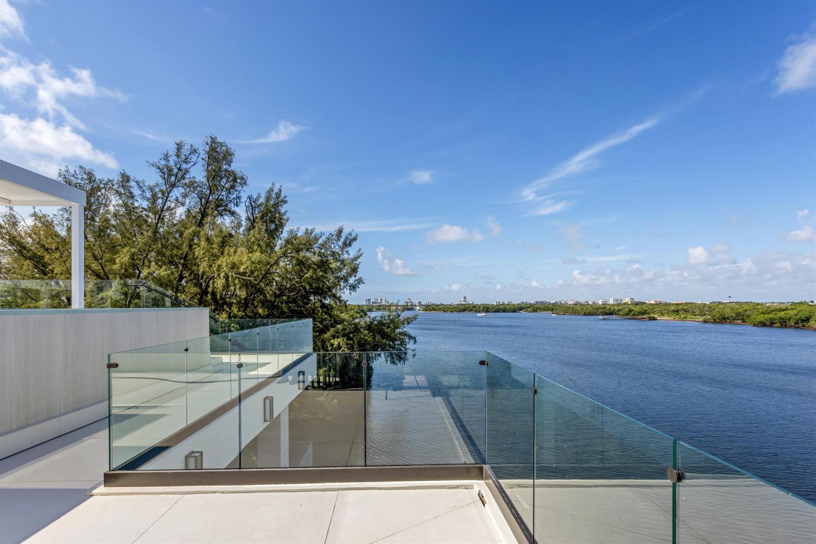 A modern balcony with glass railings overlooks a wide river and lush green trees — 900 Lago Mar Lane, Boca Raton FL 33431, BOCA RATON, FL