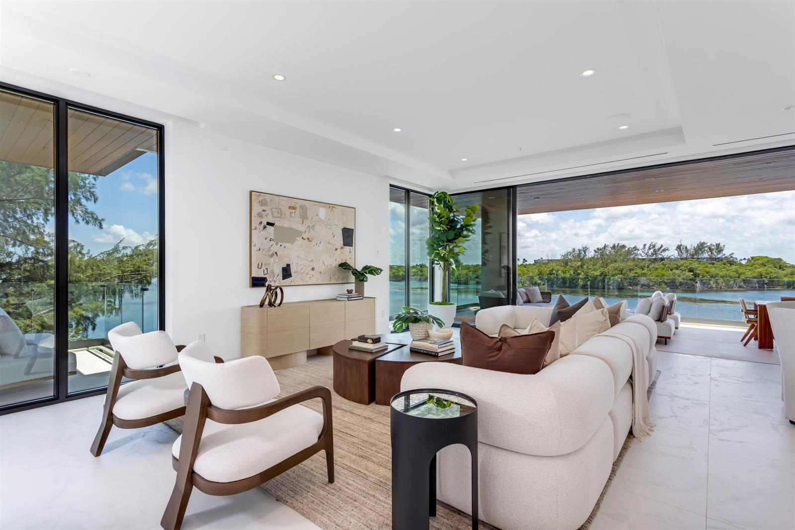 A modern living room features a white sofa, two armchairs, and floor-to-ceiling windows overlooking water — 900 Lago Mar Lane, Boca Raton FL 33431, BOCA RATON, FL