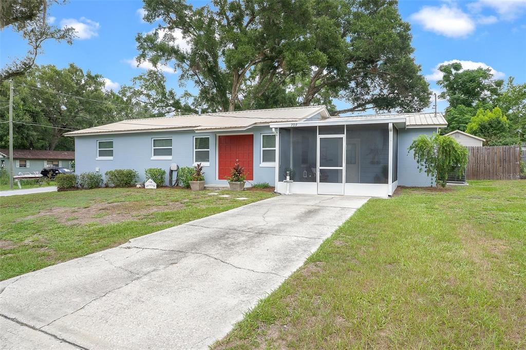 A single-story light blue house with a red front door and a screened-in porch — 709 CINDY AVENUE, FRUITLAND PARK, FL