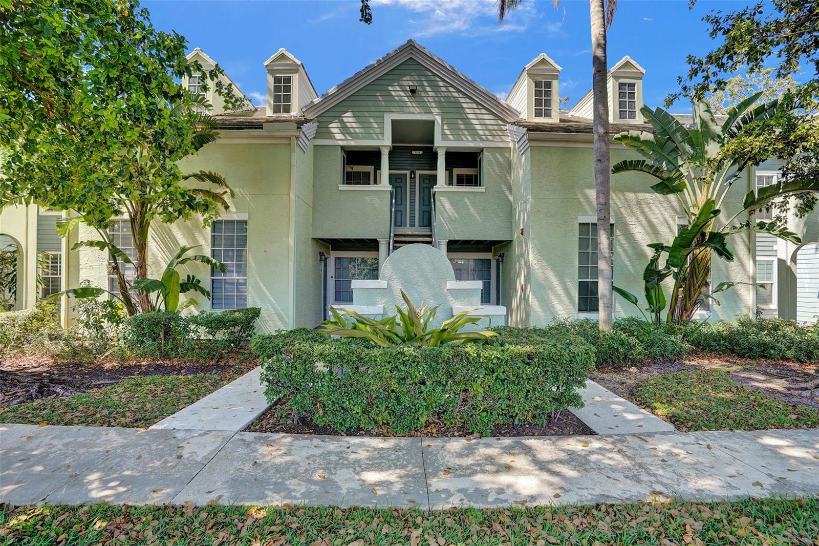 A two-story light green apartment building with a central entrance and surrounding landscaping — 1050 Crystal Way, Delray Beach FL 33444, DELRAY BEACH, FL
