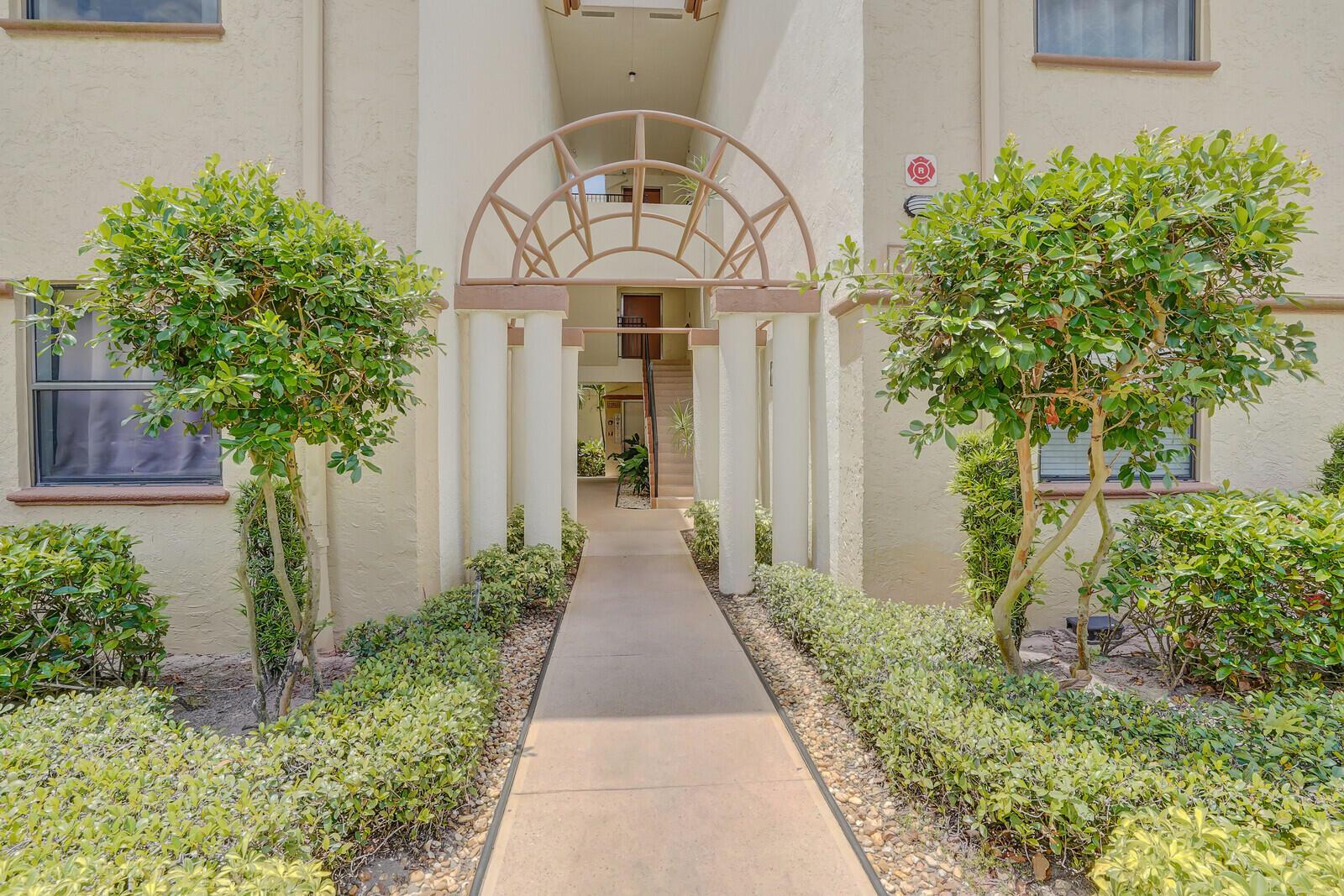 A concrete walkway leads to the arched entryway of a tan stucco apartment building — 5155 Europa Drive # I, Boynton Beach FL 33437, BOYNTON BEACH, FL