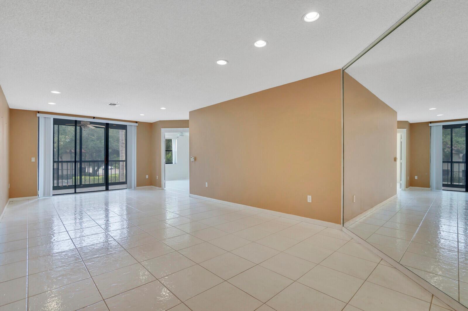 A spacious living room features beige walls, white tile flooring, recessed lighting, and a mirrored wall — 5155 Europa Drive # I, Boynton Beach FL 33437, BOYNTON BEACH, FL