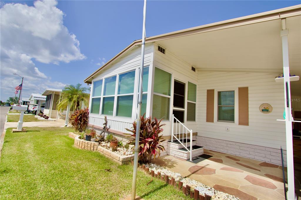 A mobile home exterior features a covered patio, a sunroom, and a landscaped garden bed — 2123 OAHU DRIVE, HOLIDAY, FL