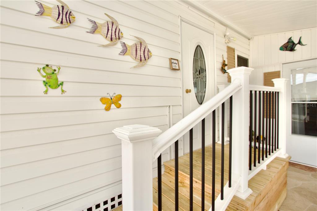 A white-sided porch features wooden steps, a white railing, and decorative wall-mounted animal figures — 2123 OAHU DRIVE, HOLIDAY, FL