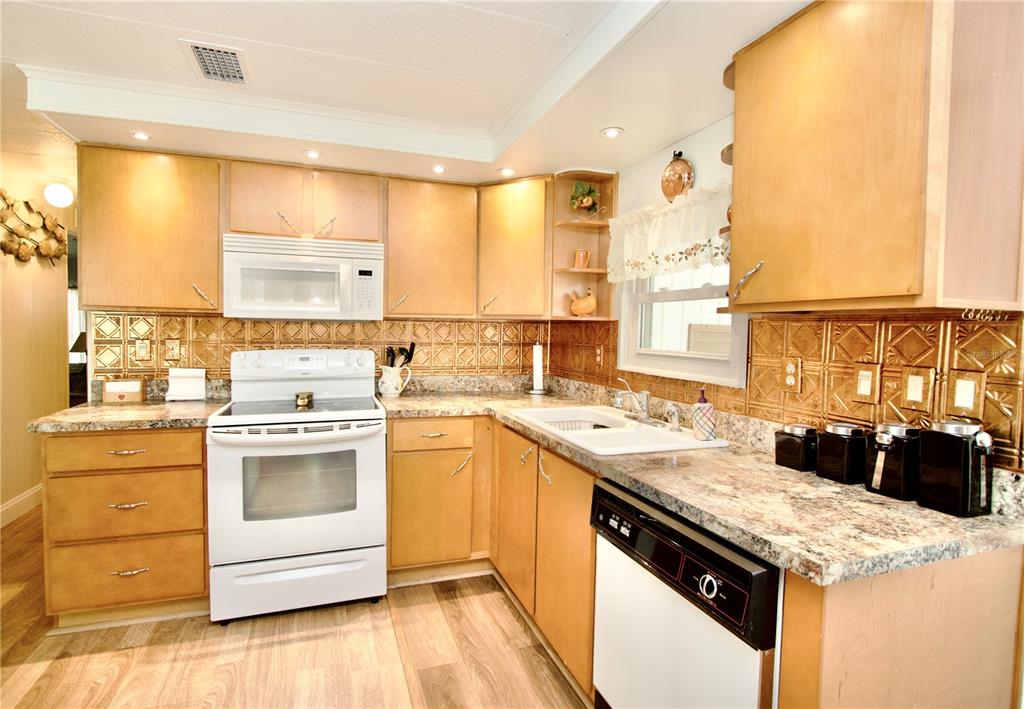 A kitchen features light wood cabinets, a white stove, a dishwasher, and a metallic backsplash — 2123 OAHU DRIVE, HOLIDAY, FL