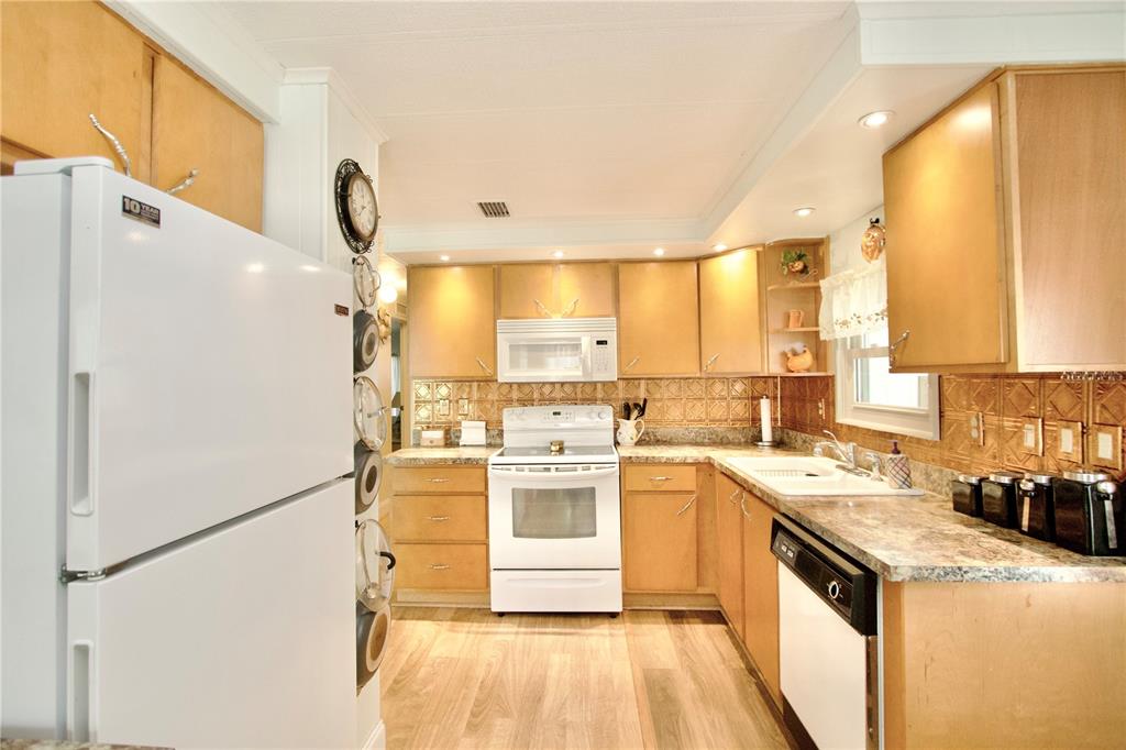 A kitchen features light wood cabinets, a white refrigerator, a white stove, and patterned backsplash — 2123 OAHU DRIVE, HOLIDAY, FL