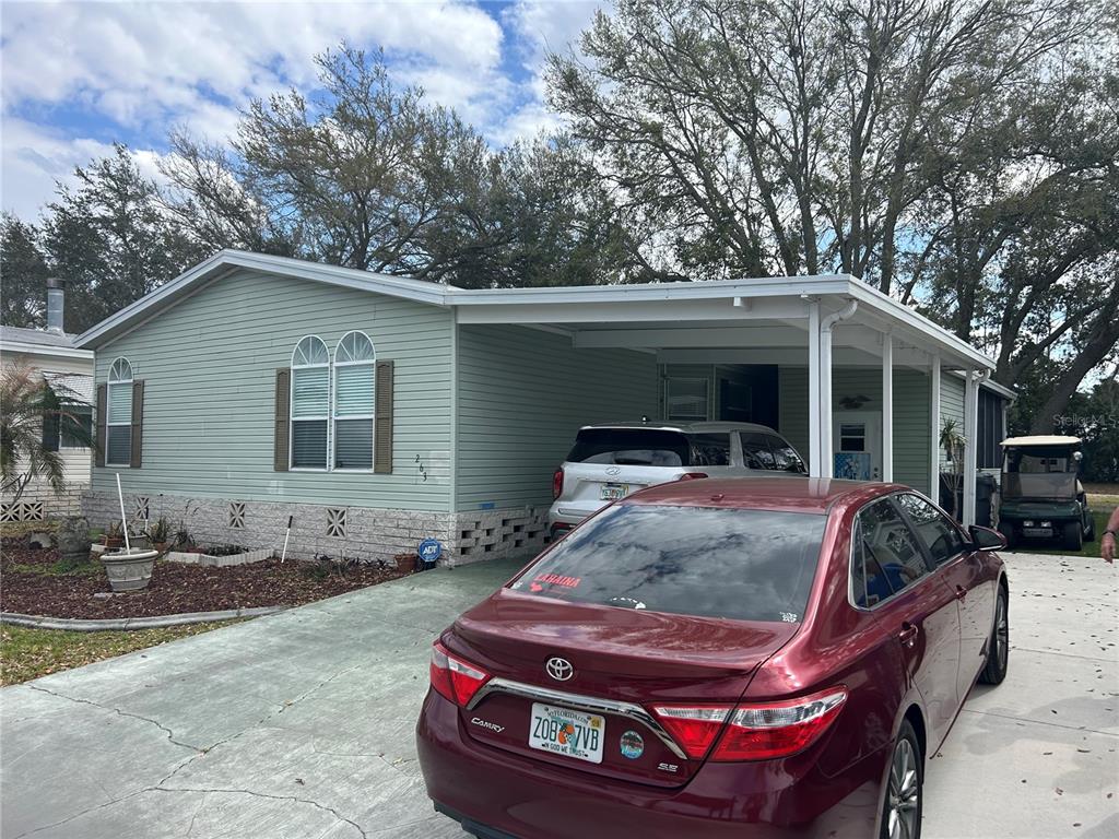 A light green manufactured home features a carport, a driveway, and two parked cars — 263 SUE AVENUE, DAVENPORT, FL