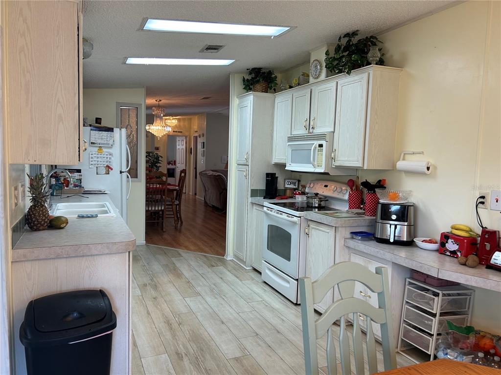 A kitchen features light-colored cabinets, white appliances, and wood-look flooring with a dining area beyond — 263 SUE AVENUE, DAVENPORT, FL