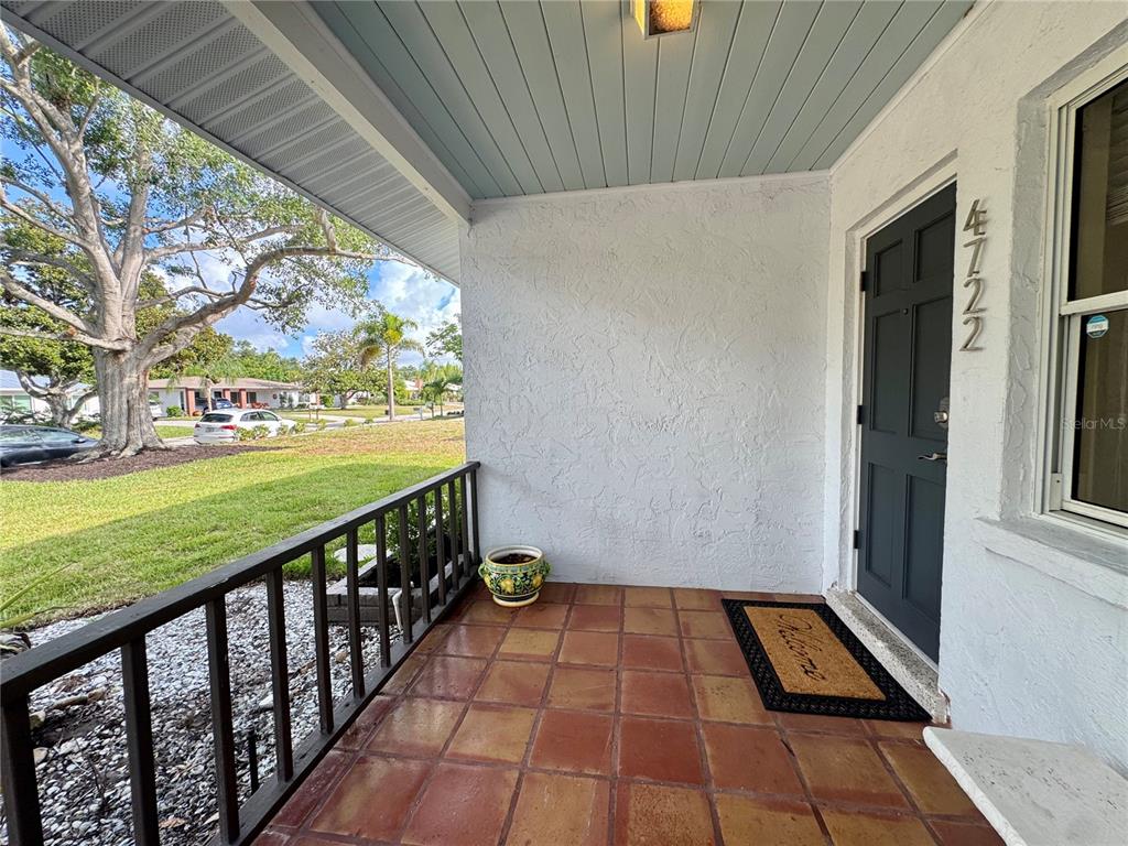 A covered front porch features terracotta tile flooring, a dark door, and a wooden railing — 4722 STEVENS DRIVE, SARASOTA, FL