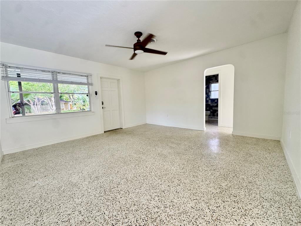 A bright, empty room features white walls, a ceiling fan, and speckled terrazzo flooring — 4722 STEVENS DRIVE, SARASOTA, FL