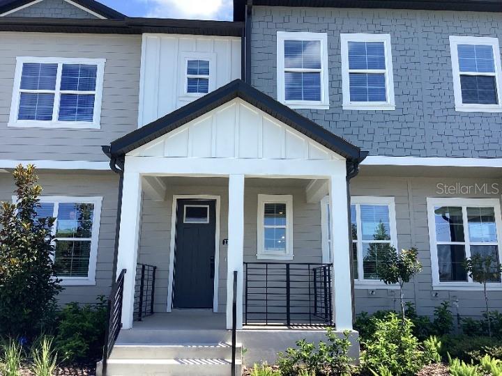 The exterior of a two-story townhouse features gray siding, a covered porch, and multiple windows — 13419 LEMON ORCHARD BEND, WINDERMERE, FL