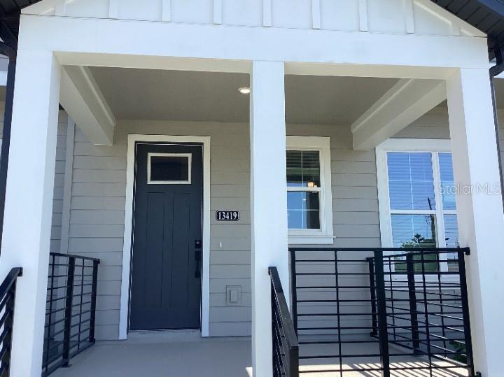 A covered front porch features a dark door, horizontal siding, and black metal railings — 13419 LEMON ORCHARD BEND, WINDERMERE, FL