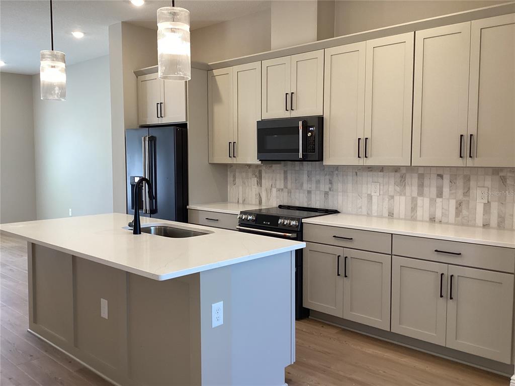 A modern kitchen features light gray cabinets, white countertops, a central island, and black appliances — 13419 LEMON ORCHARD BEND, WINDERMERE, FL